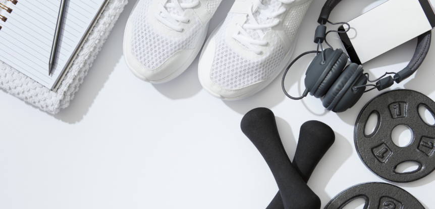 How to Maintain a Consistent Exercise Routine, white background with notebook, white gym shoes, gray headphones, black dumbells and weights.