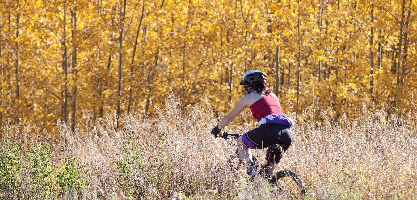 How to fit a bike helmet. Woman in red tank top wearing a helmet and riding through tall grasses.