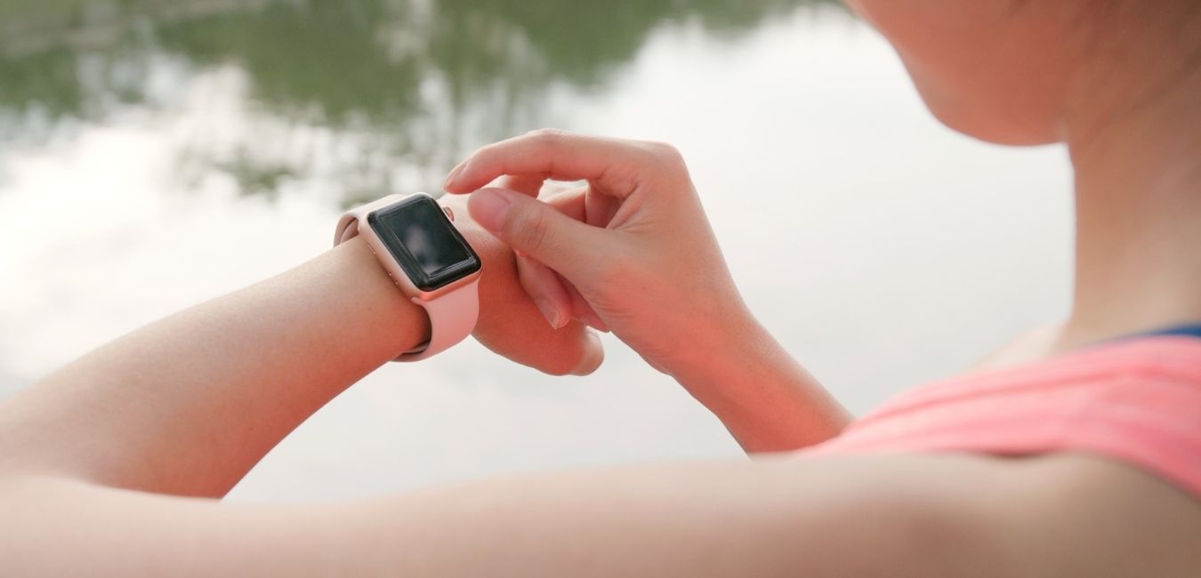 Putting Safety First Means You Never Have to Think About It. Why you should get a Road ID. Woman wearing a pink tank top checking her pint fitness watch.