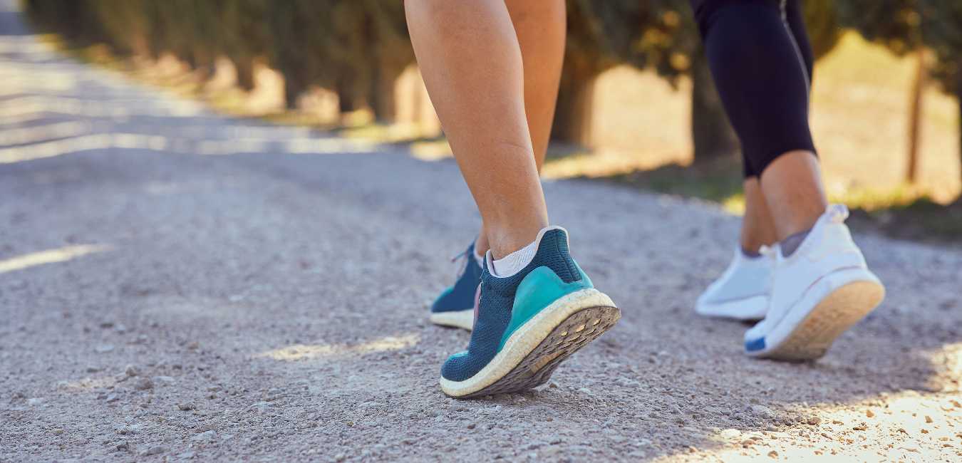 Fitness Challenges Suck. But Challenging Yourself is the Smartest Move You Can Make. Closeup of two women in workout shoes walking along a path.